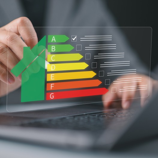 Themenbild für Energieeffizienz: Hand zeigt auf Energieeffizienzskala A bis G auf transparentem Display über Laptop